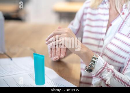 Les mains féminines frottent la crème à la main au-dessus du bureau Banque D'Images