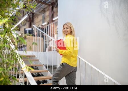 Blonde femme monter les escaliers, tenant le carnet rouge Banque D'Images