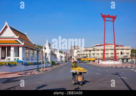 Un vendeur de bananes avec son poussette passe le célèbre Giant Swing (Sao-Ching-Cha) et Wat Suthat (à gauche) à Bangkok, Thaïlande Banque D'Images