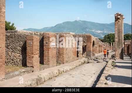 Les touristes marchent le long des rues pavées entre les bâtiments ruinés de l'ancienne ville de Pompéi, en Italie Banque D'Images