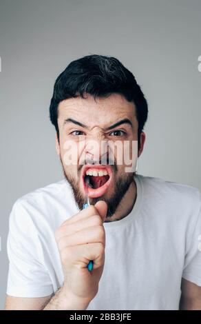 Jeune homme isolé en arrière-plan. Photo verticale des dents de nettoyage de type barbu. Utilisation de la brosse à dents avec du dentifrice. Oran et soins dentaires Banque D'Images