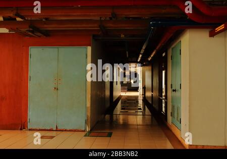 Couloir silencieux dans un bâtiment à côté de la porte bleue en bois en décomposition, avec des conduites d'eau rouges installées au plafond Banque D'Images