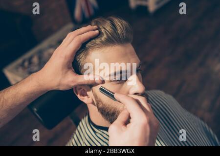 Gros plan sur le travail d'un coiffeur pour un jeune homme blond séduisant au salon de coiffure. Il fait le styling de sa barbe, la rasant avec droit Banque D'Images