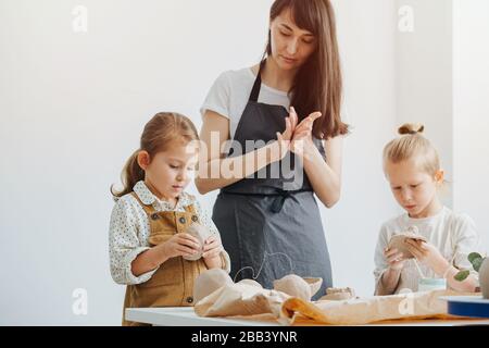 Concept de mentorat. Attirer des enfants avec la modélisation de l'argile, une jeune femme et des enfants font des plaques ensemble Banque D'Images