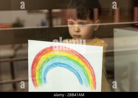 Un petit enfant inspirant tenant un dessin d'un arc-en-ciel à travers la fenêtre Banque D'Images