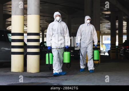 Hommes en coronavirus costumes tenant des produits chimiques de désinfection à l'extérieur Banque D'Images