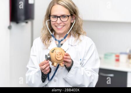 Médecin souriant en examinant la piggybank avec le stéthoscope . Banque D'Images