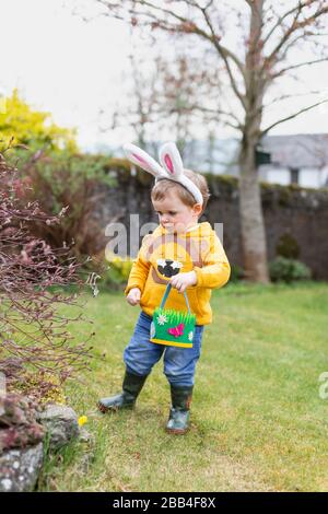 Garçon extérieur dans le jardin portant des oreilles de lapin pour la chasse aux œufs de Pâques, Écosse, Royaume-Uni Banque D'Images