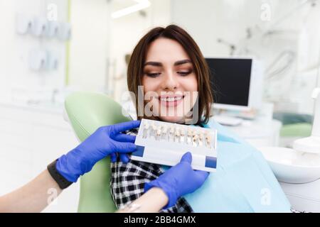 Le dentiste et son patient choisissent un ton de veneurs. Le médecin dentaire montre une palette de nuances pour les dents Banque D'Images