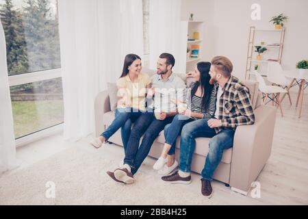 Deux couples heureux sont assis sur un canapé confortable à la villa à la maison de la fête, ayant une belle conversation, partager les histoires de la vie et embrasser, boire Banque D'Images