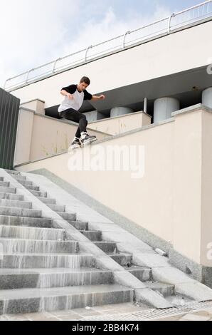 Beau jeune skateur professionnel de patinage sur roulettes sur la rue à l'extérieur. Bâtiments urbains avec vue sur le blanc. Lumière du jour. Banque D'Images