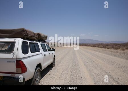 La longue route de terre sur les plaines de Namibie s'étend devant un 4 x 4 avec des tentes de toit pour le camping Banque D'Images