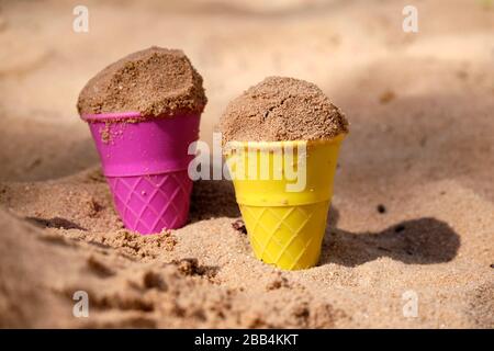 Gros plan de deux moules de sable colorés en forme de cônes de glace avec du sable dedans il colle dans le sable d'une fosse de sable un jour ensoleillé avec des ombres Banque D'Images