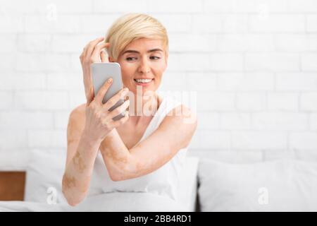 Femme d'âge moyen qui touche les cheveux souriant regardant dans le téléphone portable Banque D'Images