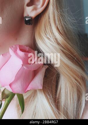 Gros plan vertical d'une femme blonde portant un contour d'oreille avec une perle noire tenant une rose rose Banque D'Images