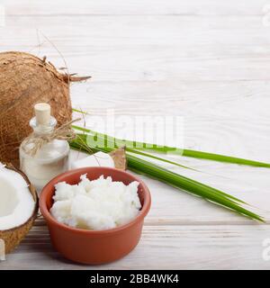 Arrière-plan de la noix de coco, noix de coco, l'huile dans un bol d'argile et de verre sur une table en bois blanc Banque D'Images