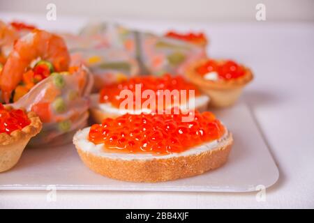 Du caviar rouge frais sur les sandwichs au pain sur la plaque. Tartelettes avec caviar rouge sur l'arrière-plan. Banque D'Images