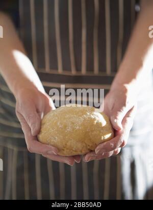 image de gros plan de la personne qui tient une boule de pâtes maison à pétrir portant un tablier rayé Banque D'Images