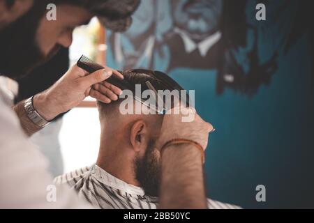 Coiffeur dans une casquette coupe les cheveux à un gars barbu Banque D'Images