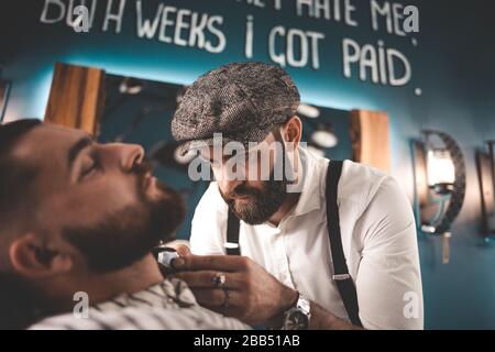 Coiffeur élégant en casquette fait une barbe coupée à un jeune boxeur Banque D'Images