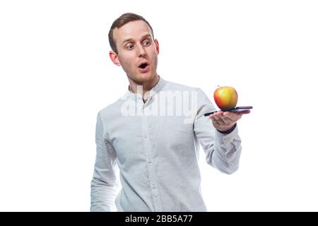 Homme d'affaires caucasien tenant un téléphone mobile en noir et tenant une pomme rouge-jaune. Il porte une chemise. Portrait émotionnel. Isolé sur la merde Banque D'Images