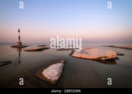 plage de sirmione la nuit et coucher de soleil sur le lac de Garde avec rochers plats sur la plage et l'eau et le soleil dedans l'horizon Banque D'Images