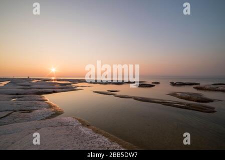 plage de sirmione la nuit et coucher de soleil sur le lac de Garde avec rochers plats sur la plage et l'eau et le soleil dedans l'horizon Banque D'Images