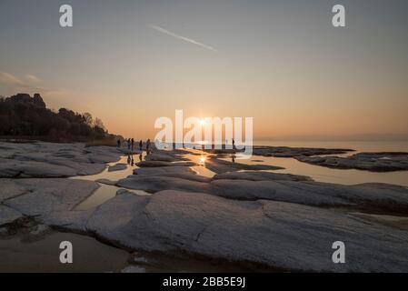 plage de sirmione la nuit et coucher de soleil sur le lac de Garde avec rochers plats sur la plage et l'eau et le soleil dedans l'horizon Banque D'Images