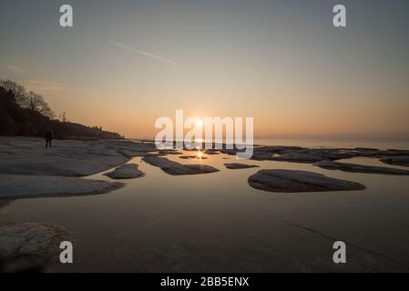 plage de sirmione la nuit et coucher de soleil sur le lac de Garde avec rochers plats sur la plage et l'eau et le soleil dedans l'horizon Banque D'Images