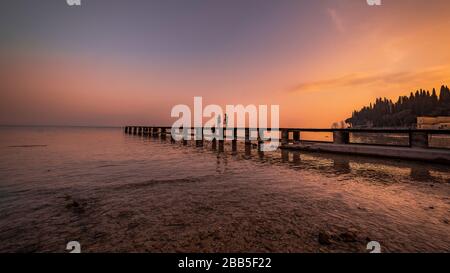 plage de sirmione la nuit et coucher de soleil sur le lac de Garde avec rochers plats sur la plage et l'eau et le soleil dedans l'horizon Banque D'Images