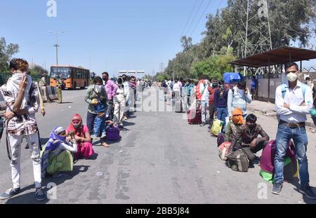 Les travailleurs migrants attendent dans des files d'attente pour embarquer dans des autobus dans leurs villages de l'Uttar Pradesh (UP) à un arrêt de bus temporaire établi à New Delhi le dimanche 29 mars, Banque D'Images