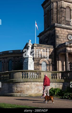 L'homme en veste rouge marche son chien devant une statue à l'extérieur de l'église Saint-Chads de Shrewsbury un matin lumineux au début du printemps. Banque D'Images