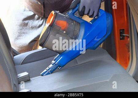 Aspirateur entre les mains du conducteur. Nettoyage de l'intérieur de l'automobile avec aspirateur bleu, fermeture. Les sièges en textile de voiture sont régulièrement nettoyés. Banque D'Images