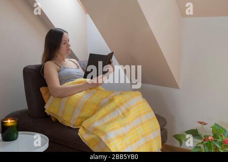 Jeune femme caucasienne lisant un livre sur un entraîneur par la fenêtre. Des recoins confortables et un concept de séjour à la maison Banque D'Images