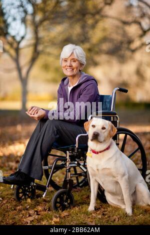 Portrait of a smiling woman dans un fauteuil roulant à côté de son chien dans un parc. Banque D'Images