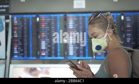 Femme caucasienne à l'aéroport de Suvarnabhumi avec masque médical protecteur. Carte d'information de vol. Utilisez un smartphone mobile. Cov-2-SRAS-19. Banque D'Images