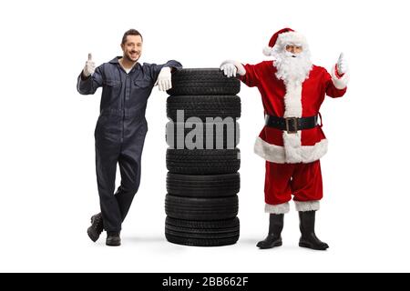 Portrait complet d'un mécanicien automobile et du Père Noël avec une pile de pneus montrant des pouces isolés sur fond blanc Banque D'Images