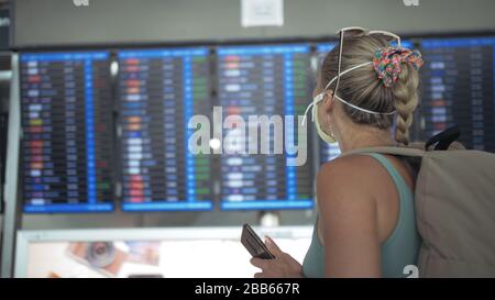 Femme caucasienne à l'aéroport de Suvarnabhumi avec masque médical protecteur. Carte d'information de vol. Utilisez un smartphone mobile. Cov-2-SRAS-19. Banque D'Images