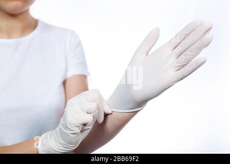 Fille paramédic met des gants médicaux blancs sur les mains. Protection contre les germes et les virus. Elle est dans un T-shirt blanc sur un fond blanc. Banque D'Images