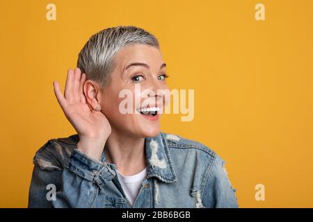 Concept de commérages. Curieuse dame mûre tenant la main près de l'oreille, à l'écoute des informations Banque D'Images