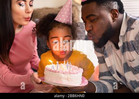 Les parents internationaux avec fille soufflent des bougies Banque D'Images