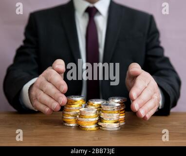 Un concept d'affaires d'un homme d'affaires demandant une pile d'argent ou protégeant ses actifs en protégeant une pile d'argent avec ses mains Banque D'Images