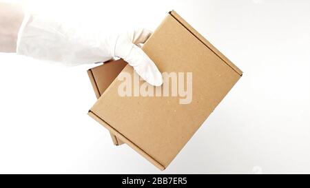 Les mains de coursier dans des gants médicaux blancs en latex fournissent des colis dans des boîtes en carton marron à la porte pendant l'épidémie de coronovirus, COVID-19.Safe Banque D'Images