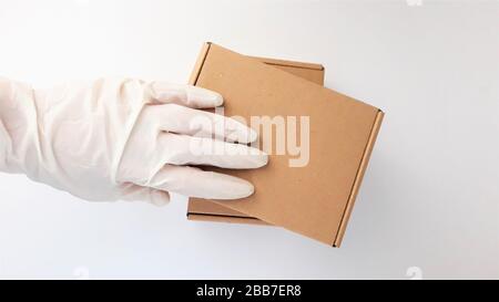 Les mains de coursier dans des gants médicaux blancs en latex fournissent des colis dans des boîtes en carton marron à la porte pendant l'épidémie de coronovirus, COVID-19.Safe Banque D'Images