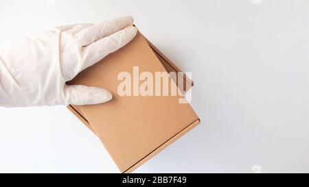 Les mains de coursier dans des gants médicaux blancs en latex fournissent des colis dans des boîtes en carton marron à la porte pendant l'épidémie de coronovirus, COVID-19.Safe Banque D'Images