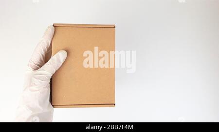 Les mains de coursier dans des gants médicaux blancs en latex fournissent des colis dans des boîtes en carton marron à la porte pendant l'épidémie de coronovirus, COVID-19.Safe Banque D'Images