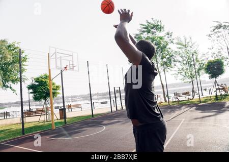 Activités en plein air. Homme africain jouant au basket-ball sur le terrain de lancer le ballon pour le triple arrière vue Banque D'Images