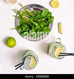 Cuisine mojito maison. Citron vert, menthe dans une assiette et des gobelets en verre avec pailles sur une table blanche Banque D'Images