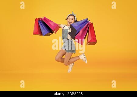 Hurry up. Acheter plus rapidement. Happy girl jump with shopping bags. Petit enfant sourire avec des sacs en papier. Préparation et célébration des fêtes. Shopping sur le black friday. Shopping d'inspiration. Traiter avec succès. Banque D'Images