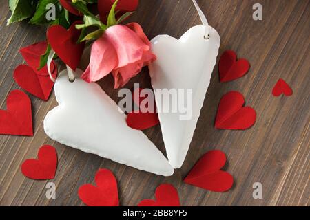 Deux coeurs blancs en porcelaine sur la table de texture en bois avec fleur rose et beaucoup de coeurs en papier rouge autour. Mariage ou signe d'amour. Pose plate. Banque D'Images